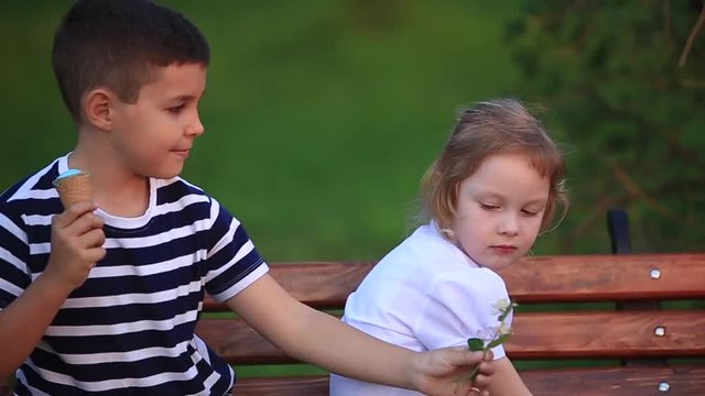 Boy eating an ice cream and sitting on the bench while girl is looking