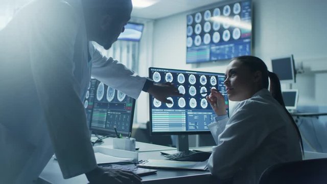 Two Scientists in the Brain Research Laboratory work on a Project, Using Personal Computer with MRI Scans Show Brain Anomalies. Neuroscientists at Work. Shot on RED EPIC-W 8K Helium Cinema Camera.