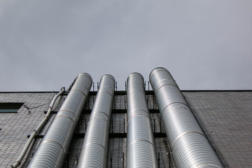 Metal ducts attached to side of drab building on smoggy day