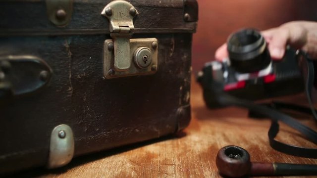 Vintage photo camera, pipe and suitcase on table.
