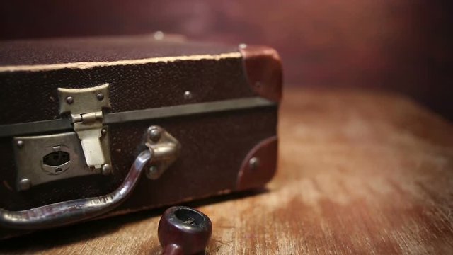 Man putting suitcase, pipe and photo camera on table.