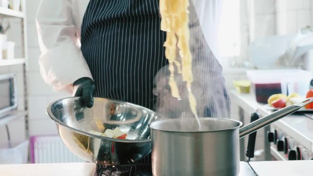 Chef taking out a boiling italian pasta with tongs in commercial kitchen.