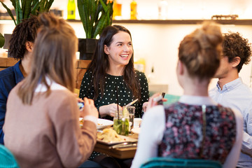 leisure and people concept - happy friends eating and drinking non-alcoholic drinks at bar or restaurant