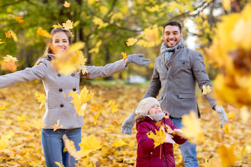 family, season and people concept - happy mother, father and little daughter playing with autumn leaves at park