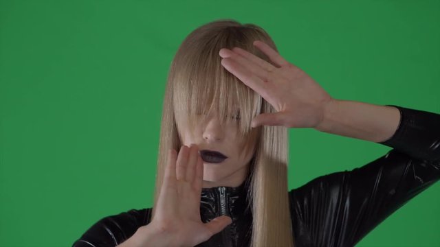 a portrait of a young blonde with bright lips, who moves her hands like a young woman from the future, a lady stands on a green background called a chromakey