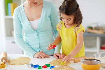 Fototapeta premium family, cooking and people concept - happy mother and little daughter with molds making cookies from dough at home kitchen