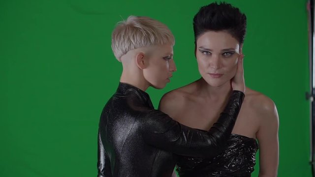 portrait of two women, blonde touch a brunette face on a green background, a lady looks like an inhuman resident, maybe they are actresses and rehearse a role for filming in the movie about the aliens