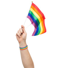 lgbt, same-sex relationships and homosexual concept - close up of male hand wearing gay pride awareness wristband holding rainbow flags
