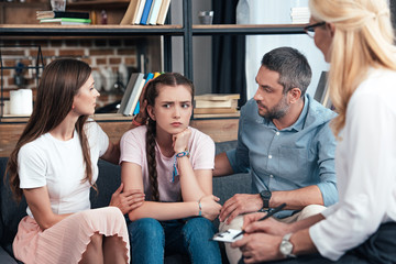 parents cheering up daughter on therapy session by female counselor in office - obrazy, fototapety, plakaty