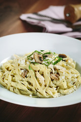 Penne pasta in tomato sauce with chicken, tomatoes decorated with parsley on a wooden table