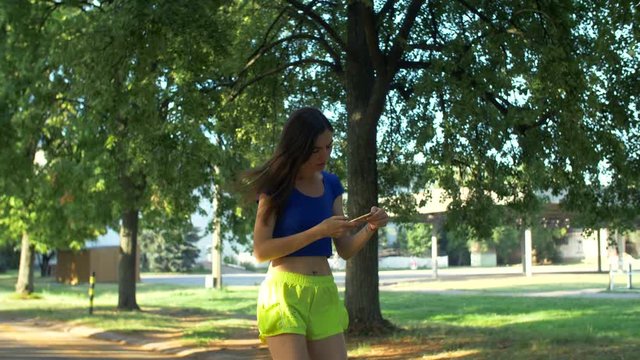 Sporty fit woman interrupted by important phone call during jogging in public park. Beautiful healthy active woman receiving a phone call during running over natural landscape background.