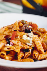 Penne pasta in tomato sauce with chicken, tomatoes decorated with parsley on a wooden table