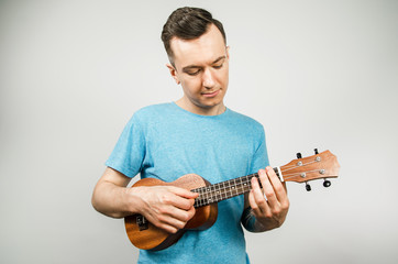 A young guy plays on a ukulele on a light background.