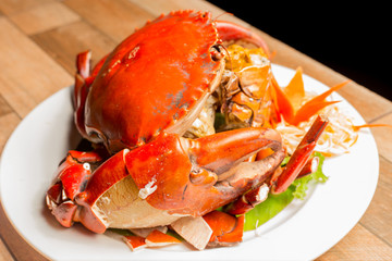 Steamed crab or Boiled crab fresh with crab's spawn in white dish showing the delicious crab's eggs inside its shell on wood table. Thai seafood.