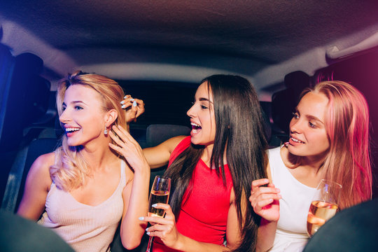 Excited girls are looking at their friend. Brunette is touching the ear of her blonde firend. There are one of beautiful earrings. Girls are sitting in car and having some fun.