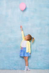 Full length. Cute little girl holding a pink balloon on a blue background.