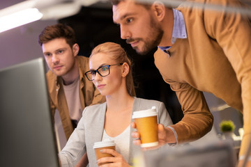 business, deadline and technology concept - coworkers with computer and takeout coffee working late at night office