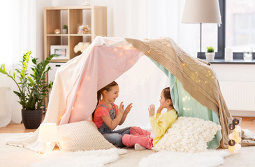 childhood, hygge and friendship concept - little girls playing clapping game in kids tent or teepee...