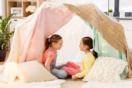 childhood, hygge and friendship concept - little girls talking in kids tent or teepee at home