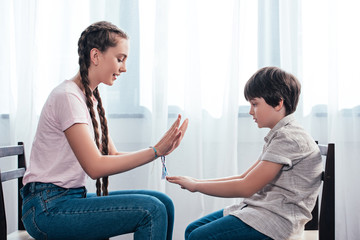 Obraz premium side view of brother and sister playing game while sitting on chairs at home
