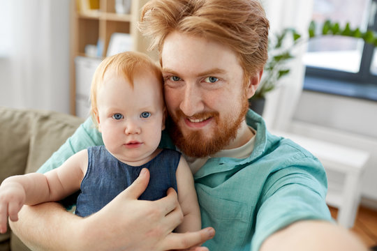 family, fatherhood and people concept - happy red haired father with little baby daughter taking selfie at home
