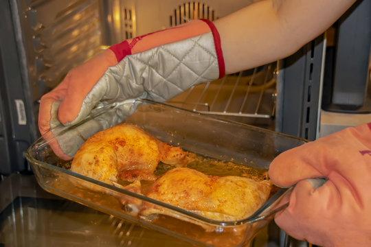 Female Hands In Heat-insulated Gloves Holding A Glass Bowl With Baked Tender Chicken Thighs