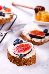 Sandwiches with creamy cheese. Ingredients: Blueberries, figs and Honey. Appetizer on a light background. Concept of a healthy breakfast.