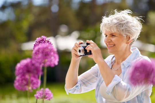 photography, leisure and people concept - happy senior woman with camera photographing flowers blooming at summer garden