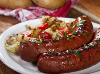 Fototapeta premium Grilled sausages on a white plate and wooden background