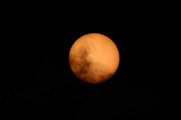 The Sun, partly obscured by clouds, photographed with a solar filter on a summer day.