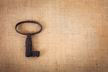 An ancient metal key on the background of sacking.