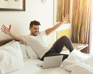 Young man using laptop while sitting on a bed
