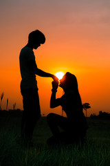 Naklejka na ściany i meble Silhouette of romantic couple on sunset background, woman kneeling Ask a married man.