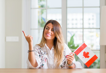 Young woman at home holding flag of Canada very happy pointing with hand and finger to the side