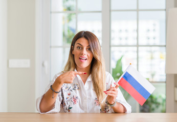 Young woman at home holding flag of Russia very happy pointing with hand and finger