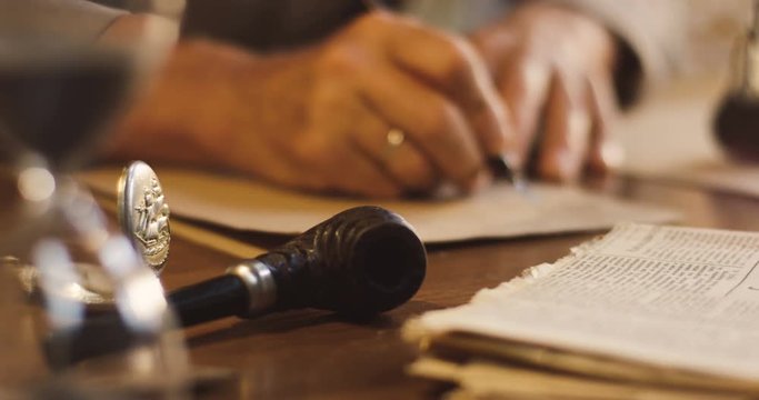 Close up of the old man stuff lying on the wooden table and blurred old male hands writing a letter with ink on the background.
