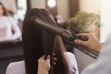 Hairdresser using curling iron at beauty salon