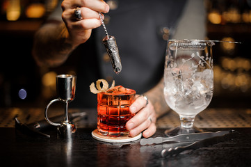 Professional bartender stirring a fresh red cocktail with a decorative spoon