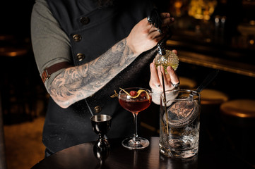 Professional bartender spraying on the delicious cocktail with a special liquid