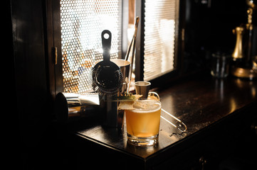 Yellow cocktail and set of essential barman equipment on the sill
