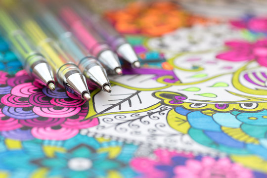 Adult coloring book, new stress relieving trend. Art therapy, mental health, creativity and mindfulness concept. Adult coloring page with pastel colored gel pen close up.