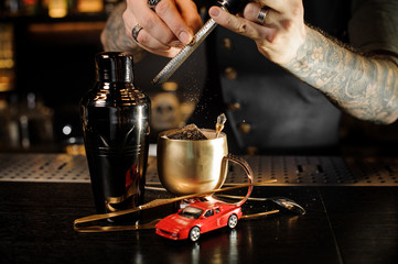 Tattooed bartender grating nutmeg to the cocktail in the copper cup