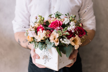 Very nice young man in a white shirt holding a beautiful fresh blossoming bouquet in a basket with roses, eustoma, eucalyptus, carnations 