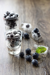 Ice cubes with berries and mint leaves  in glasses on wooden background