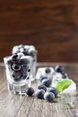 Ice cubes with berries and mint leaves  in glasses on wooden background