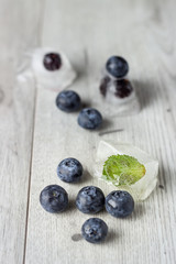 Berries frozen in ice cubes with mint on wooden table background