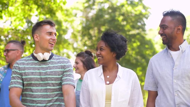 people, friendship and international concept - group of happy friends walking in park