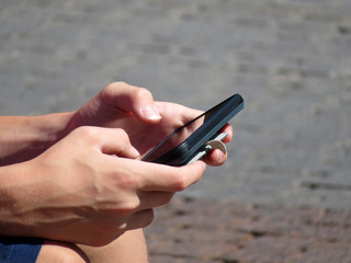 Smartphone in hand close-up. Man playing a game on a mobile phone outdoors. Summer leisure, mobile games, using smart phone