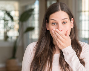 Fototapeta premium Young beautiful woman at home cover mouth with hand shocked with shame for mistake, expression of fear, scared in silence, secret concept