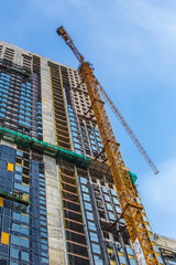 High-rise building under construction. The site with cranes against blue sky